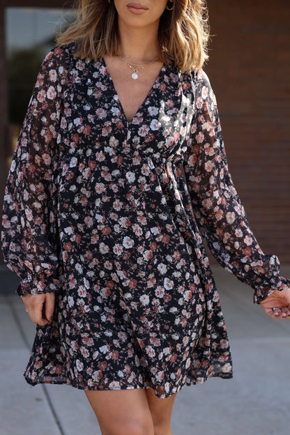 Woman in the Thalia Black Floral Print Mini Dress with pink and white flowers, standing outdoors. FINAL SALE.