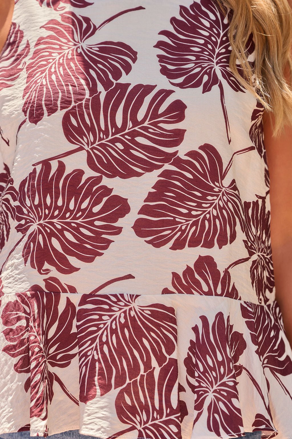 A close-up of The Palm Ruffle Top - Brown, a sleeveless top with maroon monstera leaves on light beige. FINAL SALE.