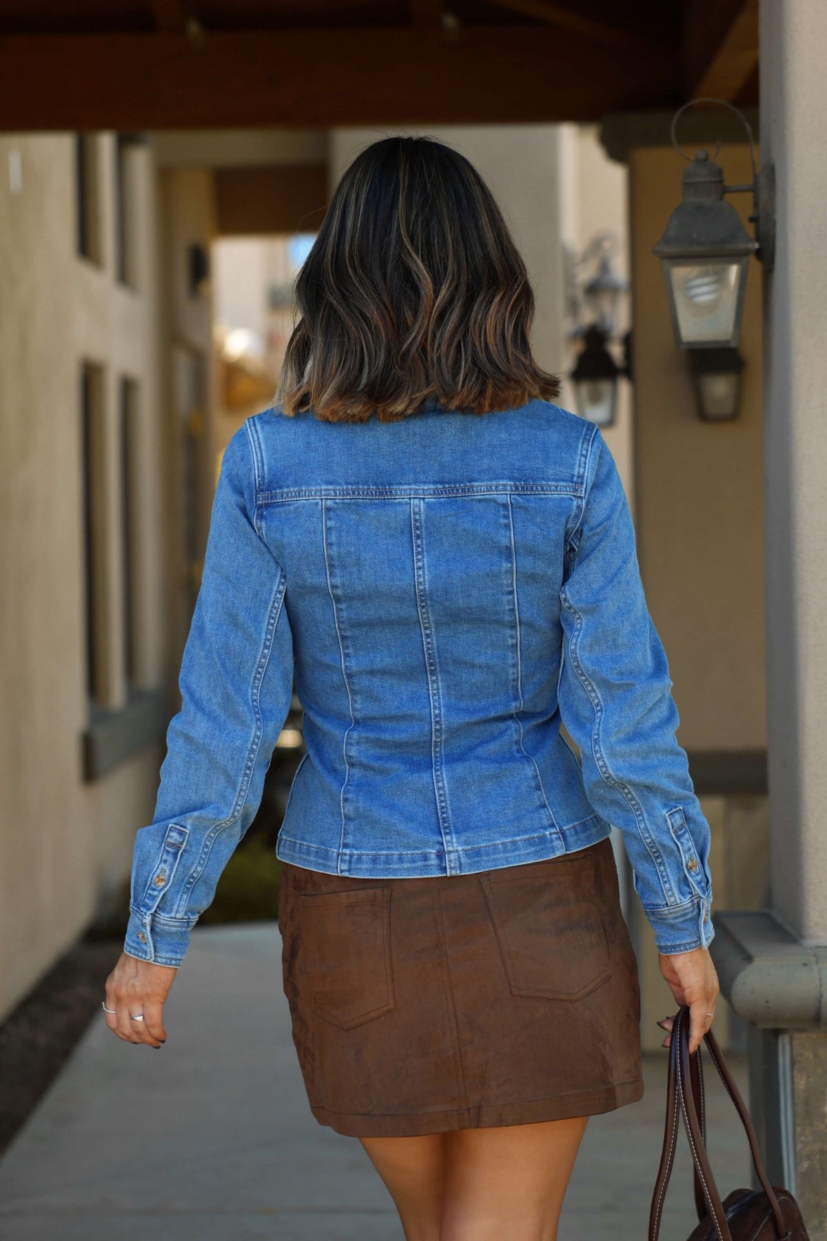 A woman wears the Thread & Supply Button Down Denim Shirt - FINAL SALE, walking outdoors with a bag.