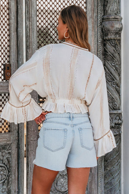 Woman with long hair in a white blouse and Vervet Light Wash Distressed Denim Shorts stands before an ornate, carved wooden door.