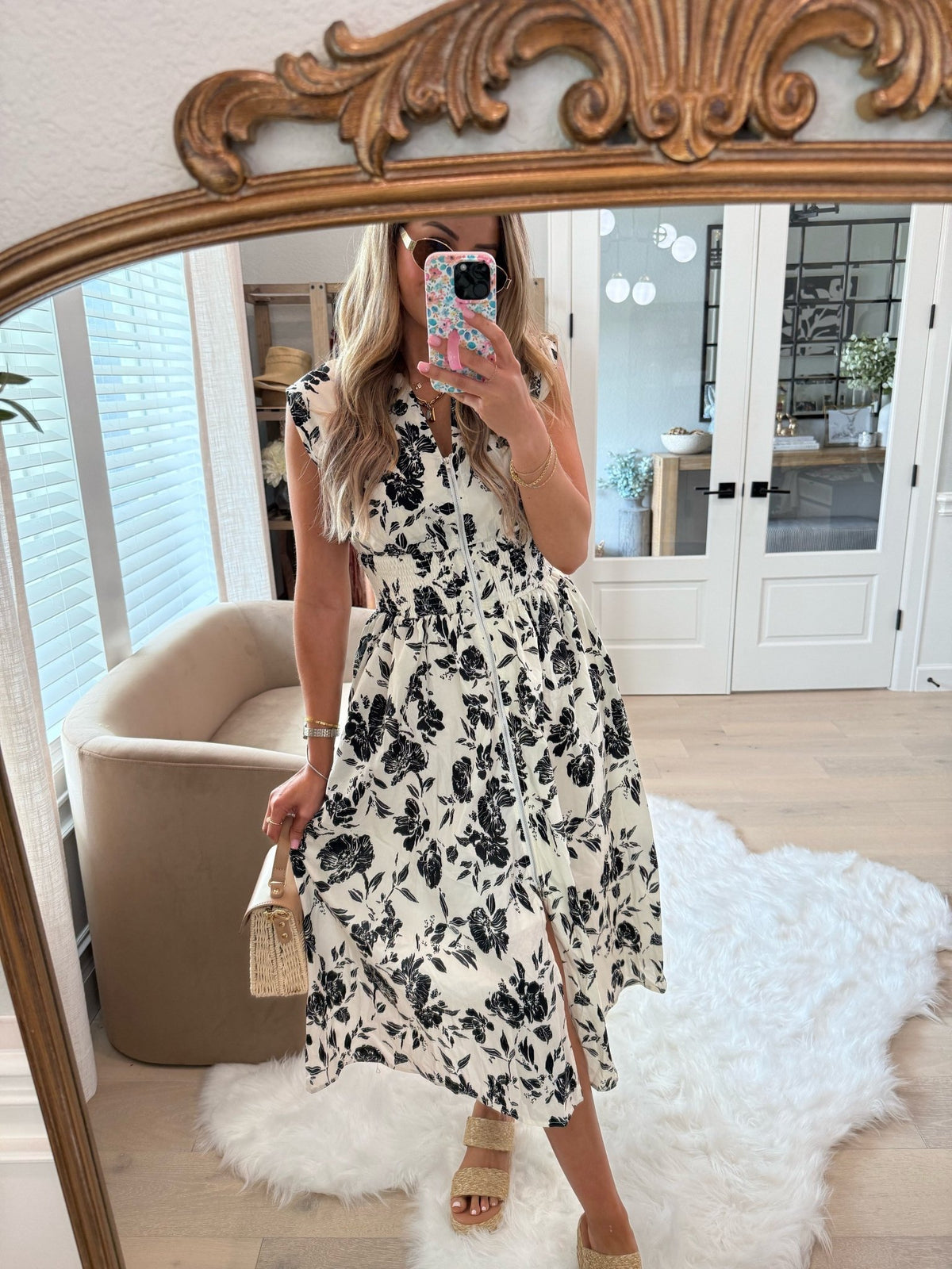 Woman in a White and Black Floral Print Smocked Midi Dress-FINAL SALE takes a mirror selfie in a bright room with rug and beige chair.