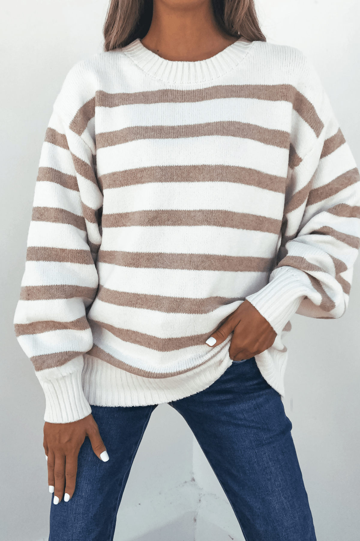 Person in a Willow Cream Stripe Ribbed Sweater and blue jeans, hand in pocket, standing against a plain light background.