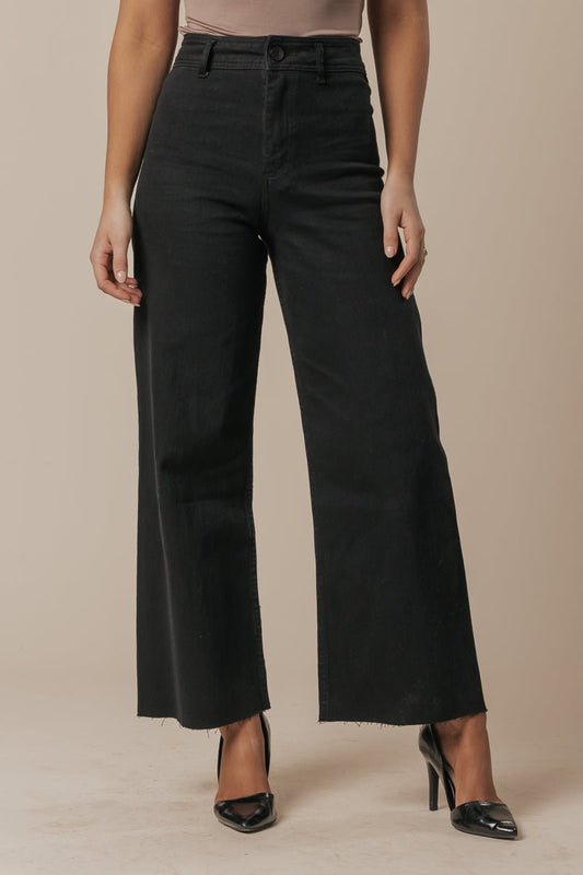 Model wears Black Straight Wide Leg Jeans with a beige top and black heels, posing against a plain background.