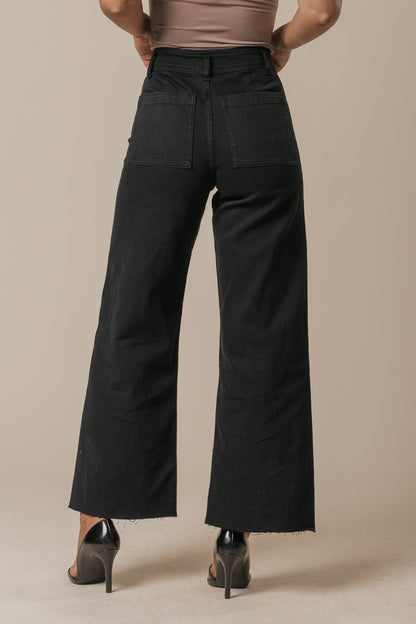 Model wears Black Straight Wide Leg Jeans with black heels, pictured from the back with hands on hips against a beige background.