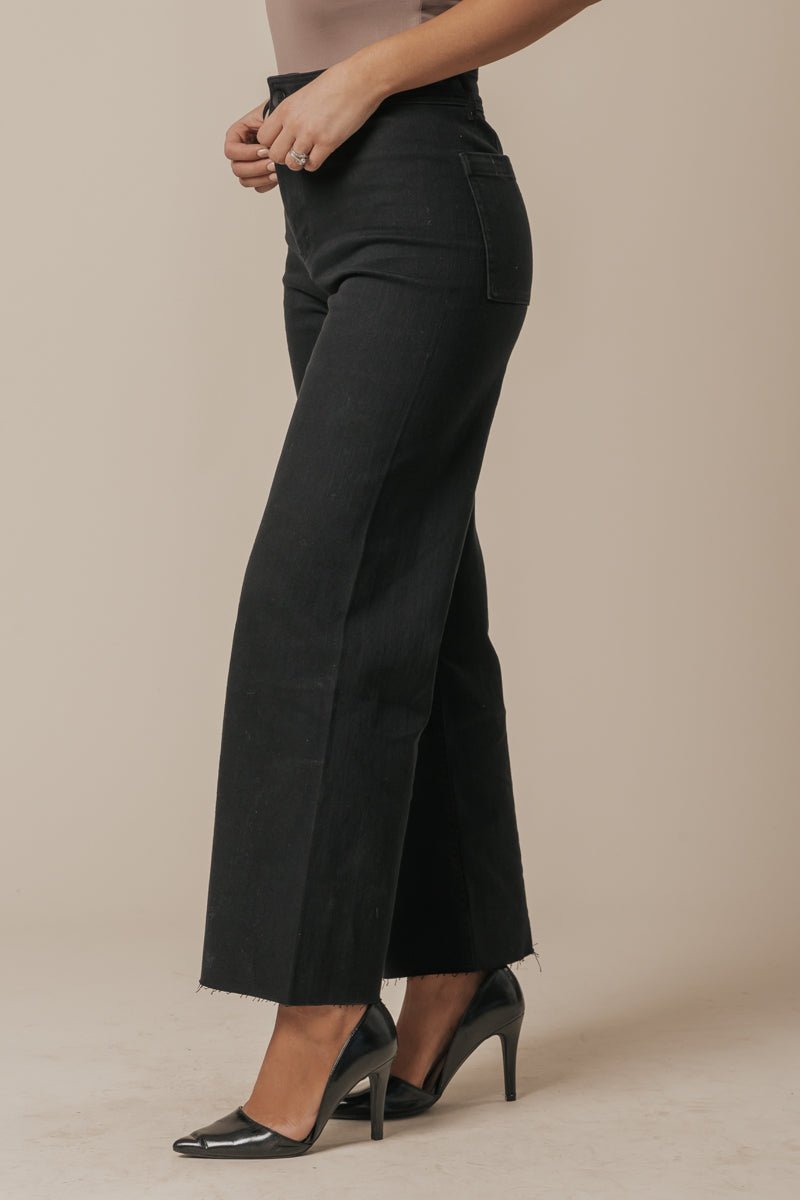 Woman models Black Straight Wide Leg Jeans with raw hems and black heels, posing sideways in front of a neutral background.