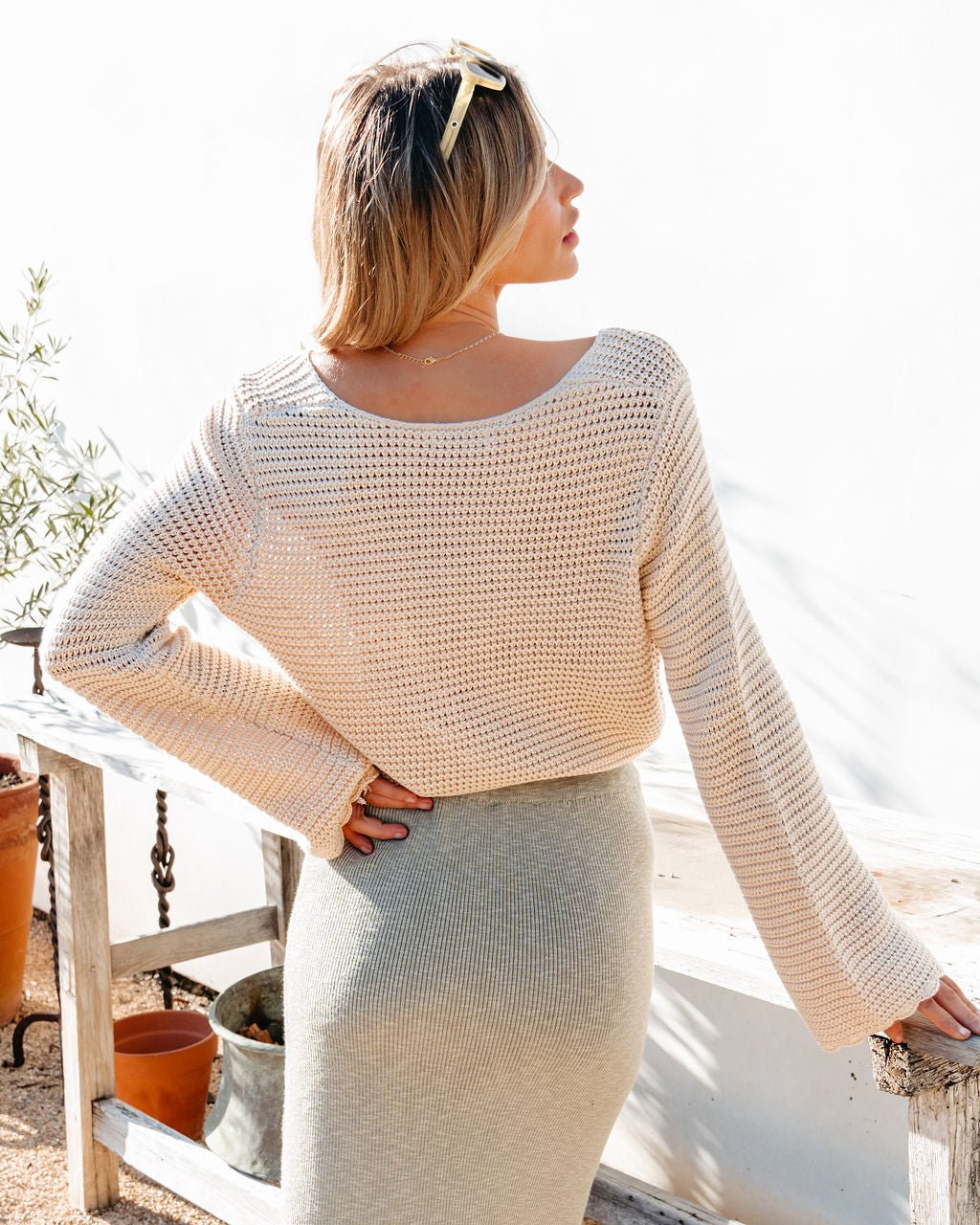 Outdoors, a woman poses by a white wall in the California Cinched Button Down Sweater—ideal for everyday style.