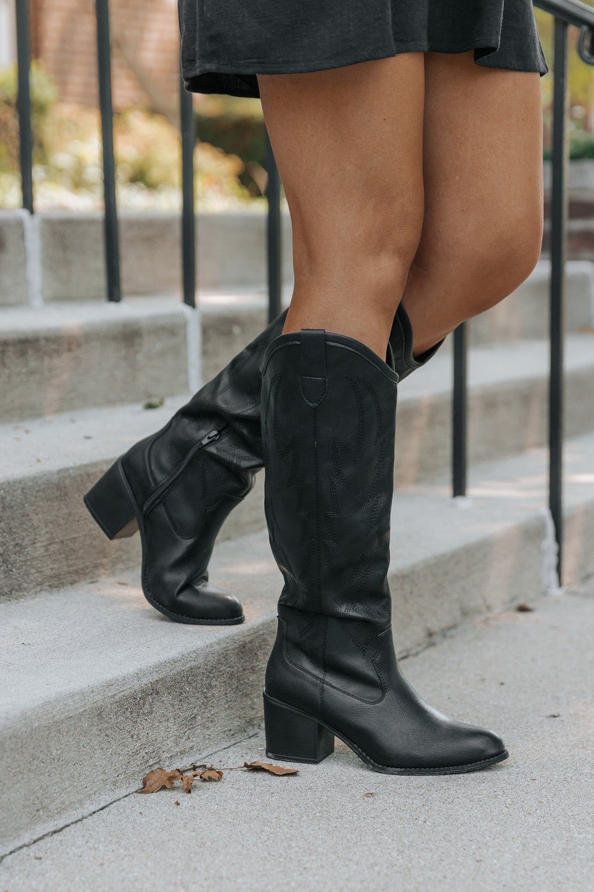 Person in Dirty Laundry Upwind Western Boots and a black skirt, standing on outdoor concrete steps with a railing.