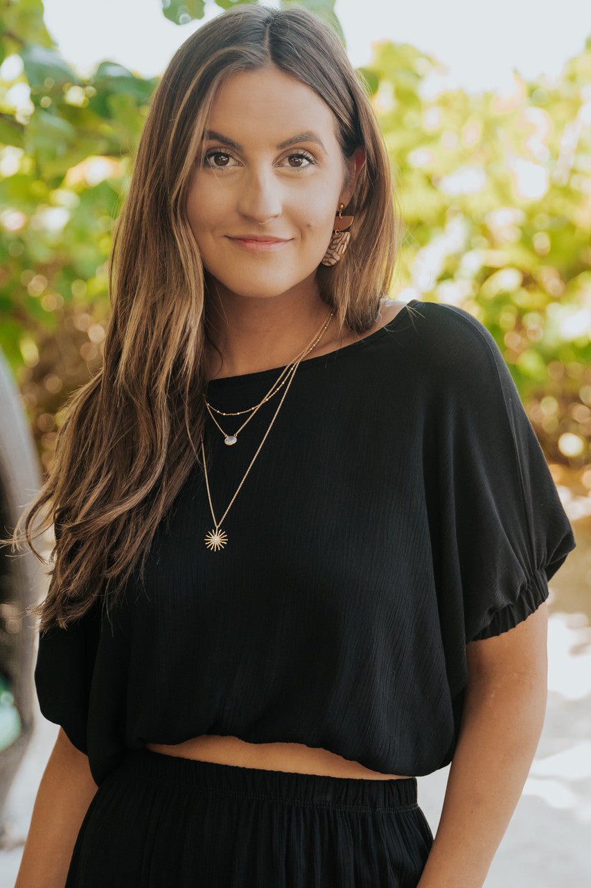 Woman with long brown hair wears the Sunrise Short Sleeve Top & Maxi Skirt Black Set outdoors, greenery in the background.