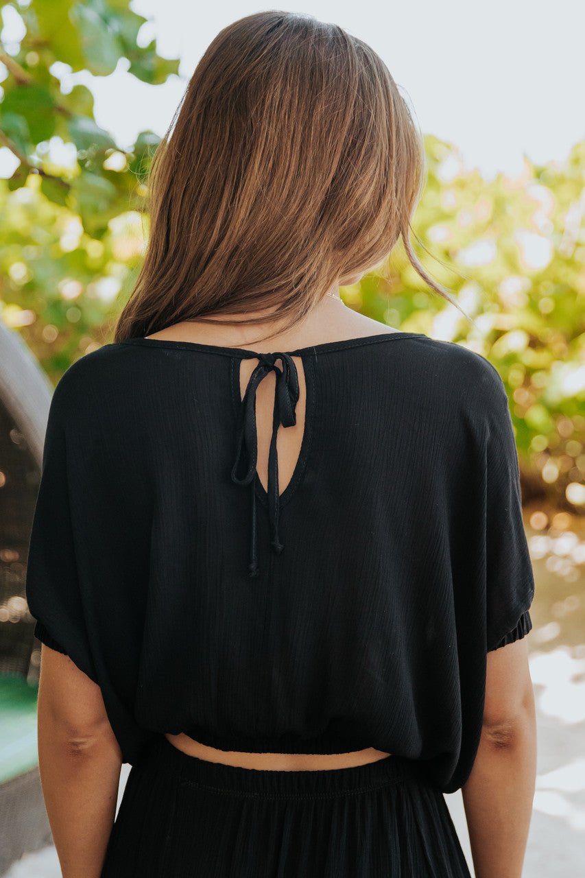A woman models the Sunrise Short Sleeve Top & Maxi Skirt Black Set-FINAL SALE outdoors; her long brown hair flows down.