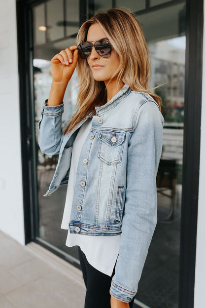 Woman in the Sweet South Faded Denim Jacket - Light Wash and sunglasses stands outside, embodying casual chic.